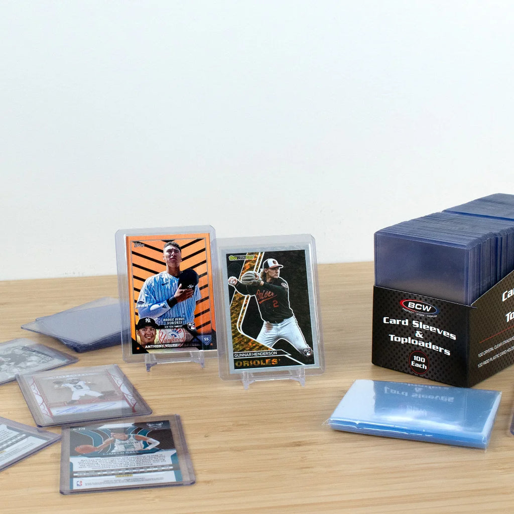 Collection of trading cards and BCW card sleeves on a wooden surface with a white background